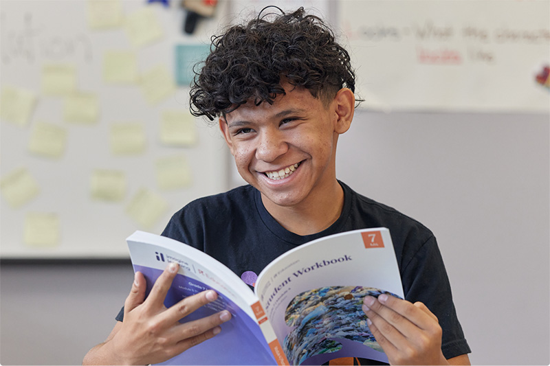 Smiling middle school student holding an Imagine Learning student workbook.