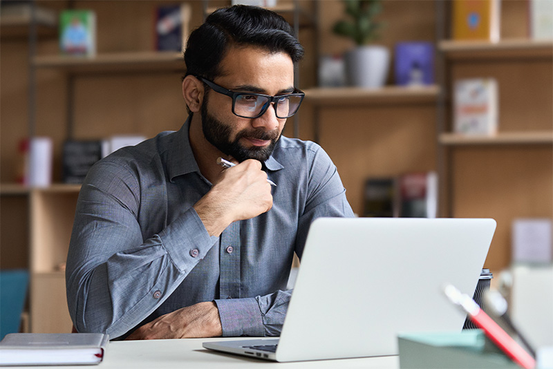 Man looking at laptop in contemplation while seated at desk