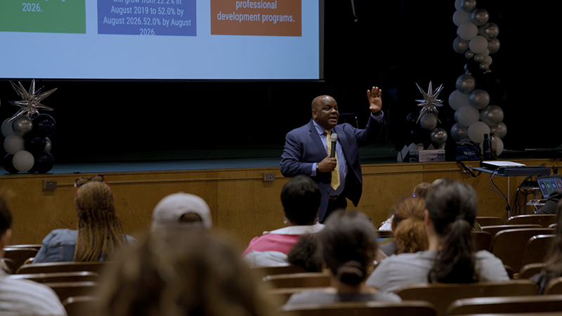 A man dynamically talks to a seated group of people.