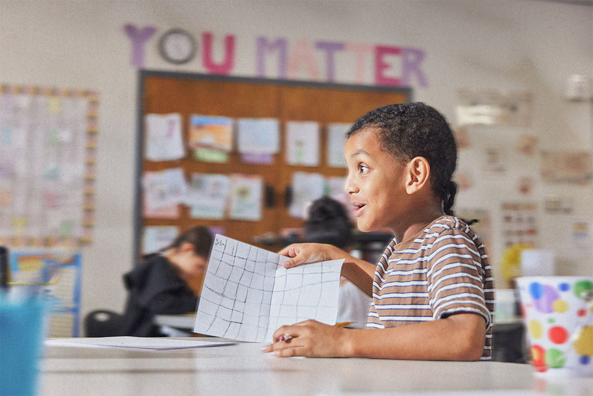 A student engages in a lesson activity, holding up his drawing.